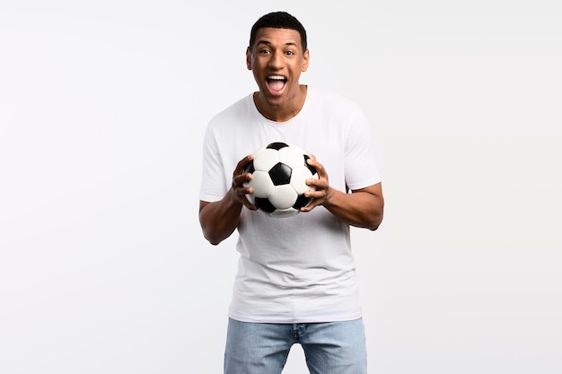 Portrait d'un bel homme tenant un ballon de football dans ses mains avec une expression positive souriante