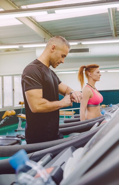 Portrait d'un bel homme vérifiant la fréquence cardiaque sur la montre lors d'un entraînement sur tapis roulant dans un centre de remise en forme. Concept sportif et technologique.