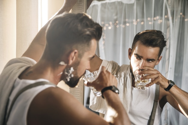 Portrait de bel homme avec un verre de whisky se regarde dans le miroir