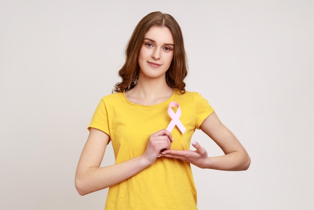 Portrait d'une belle adolescente aux cheveux bruns tenant un ruban rose devant le soutien thoracique des patients en oncologie Prise de vue en studio intérieur isolée sur fond gris