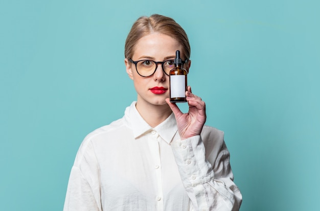 Portrait de la belle blonde en chemise blanche avec bouteille cosmétique sur mur bleu