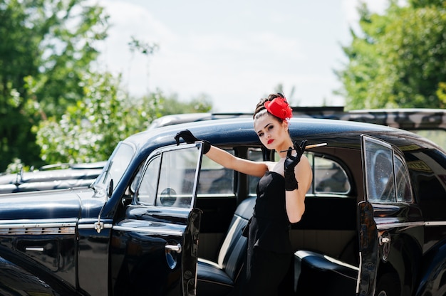 Portrait de la belle brune sexy mannequin fille avec du maquillage vif dans un style rétro près de voiture vintage avec une cigarette à la main.