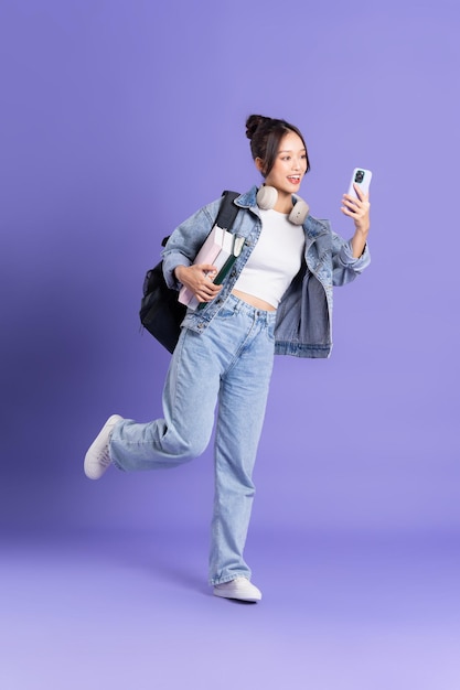 Portrait d'une belle écolière asiatique portant un sac à dos sur fond violet