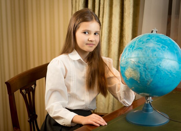 Portrait de belle écolière posant au cabinet avec globe terrestre