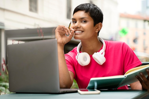 Portrait d'une belle étudiante indienne souriante étudiant, utilisant un ordinateur portable, regardant la caméra