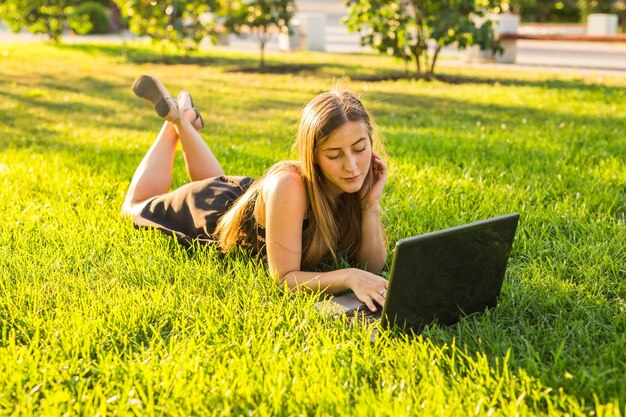 Portrait d'une belle étudiante avec ordinateur portable sur l'herbe verte dans le parc au printemps ou en été.