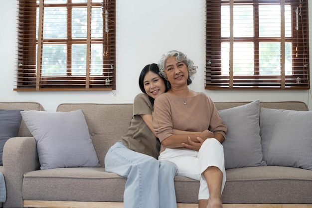 Portrait d'une belle famille asiatique jeune fille étreignant une mère plus âgée Une femme séduisante et une mère mature aînée assise sur un canapé profitent d'une activité à la maison ensemble dans le salon et sourient regarder la caméra