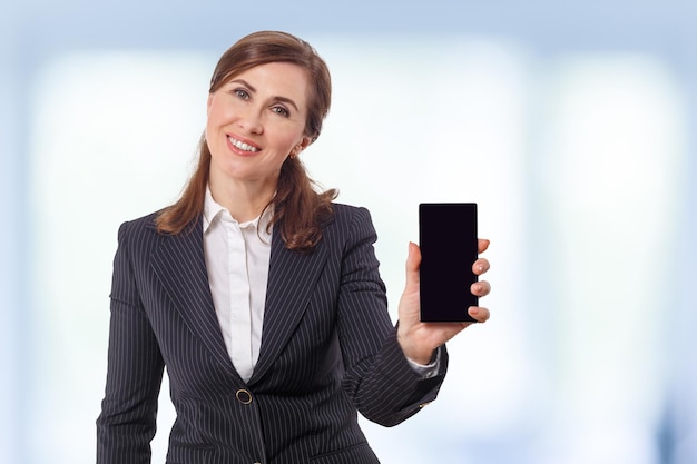 Portrait d'une belle femme d'affaires de 50 ans avec un téléphone portable au bureau