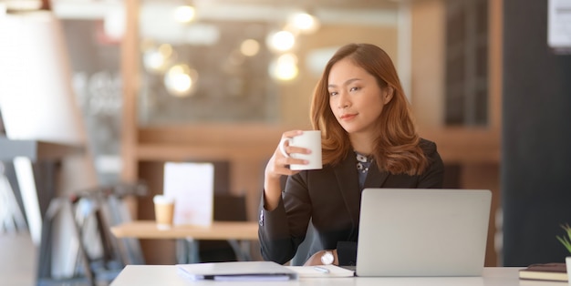 Portrait de la belle femme d'affaires asiatique, boire du café tout en travaillant sur son projet avec un ordinateur portable