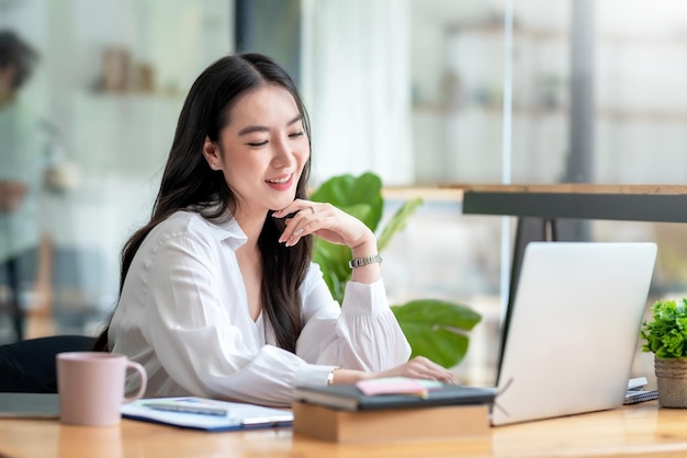 Portrait d'une belle femme d'affaires asiatique souriante, appréciez l'idée assise au bureau.