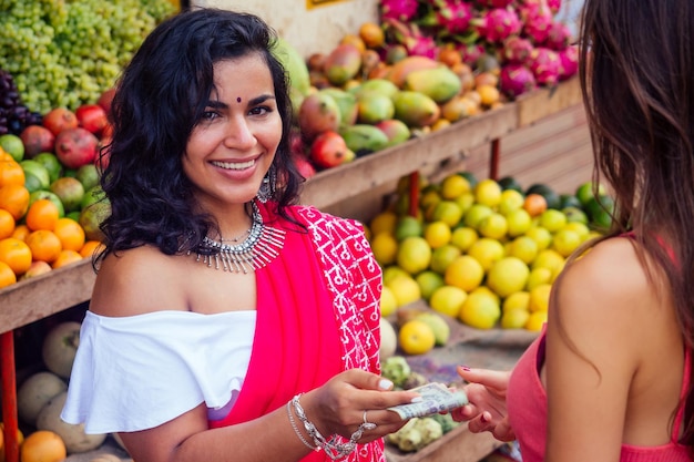 Portrait d'une belle femme d'affaires indienne traditionnelle en robe sari rouge avec un client dans la rue du marché de Delhi en Inde à mumbai. Happy girl shopper dans un supermarché fruits légumes magasin Kerala Goa.