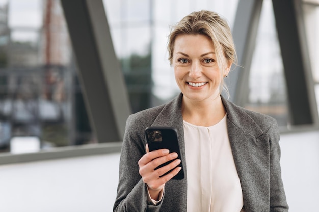 Portrait d'une belle femme d'affaires mature en costume et veste grise souriant et parlant au téléphone sur le fond urbain moderne