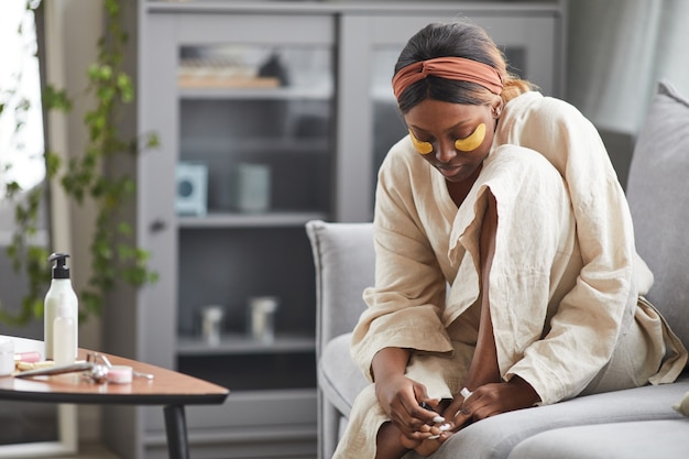 Photo portrait d'une belle femme afro-américaine profitant d'une routine de soins de la peau à la maison et faisant de la pédicure, espace de copie