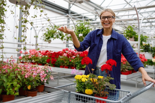 Portrait d'une belle femme d'âge moyen avec un chariot choisissant des fleurs alors qu'elle fait ses courses dans le centre du jardin