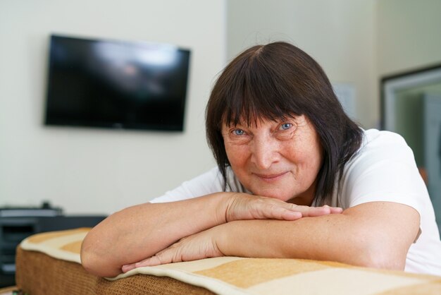 Portrait d'une belle femme âgée souriante assise sur le canapé à la maison profitant de la retraite