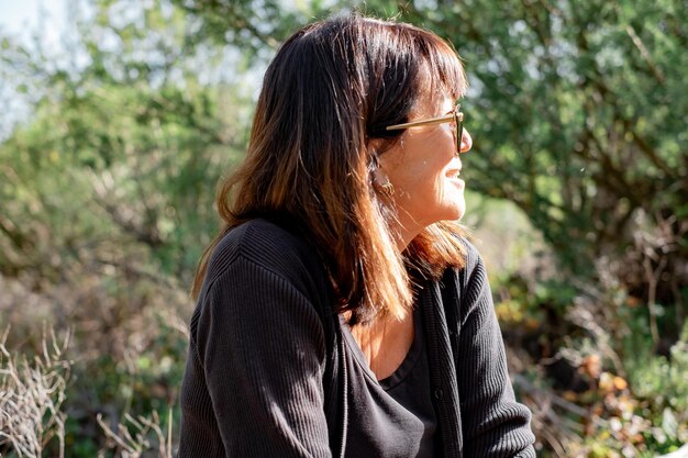 Portrait d'une belle femme âgée souriante en noir avec des lunettes de soleil assise à l'extérieur dans le parc