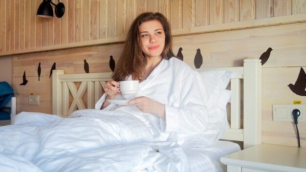 Portrait de belle femme allongée dans son lit le matin et buvant du café