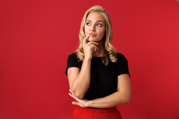 Portrait de belle femme des années 20 pensant et regardant de côté, isolé sur mur rouge