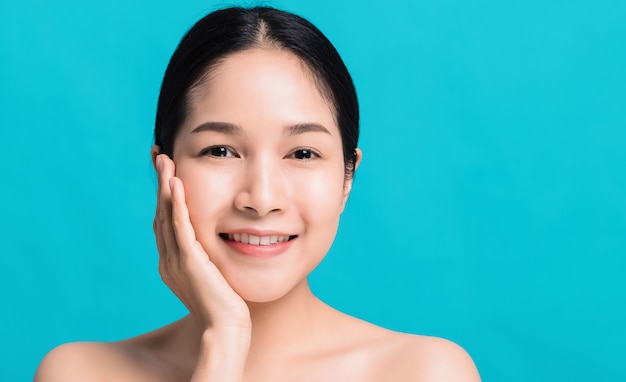 Portrait de belle femme asiatique confiante avec la main à côté du visage et souriant isolé sur fond de couleur bleue.