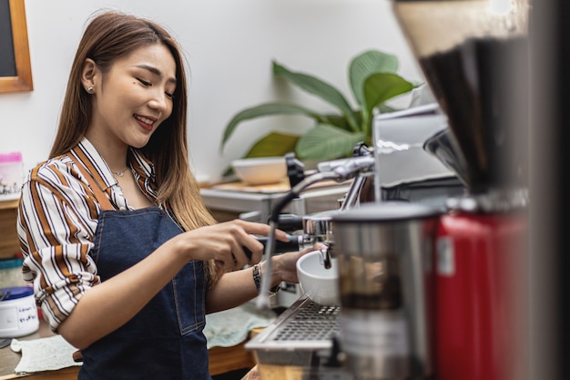 Portrait d'une belle femme asiatique dans un tablier à l'aide d'une machine à café, elle possède un café, concept d'une entreprise d'alimentation et de boissons. Gestion du magasin par une femme d'affaires.