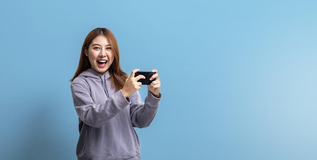 Portrait d'une belle femme asiatique jouant à un jeu de smartphone sur fond isolé concept de portrait utilisé pour la publicité et la signalisation isolée sur fond bleu espace de copie