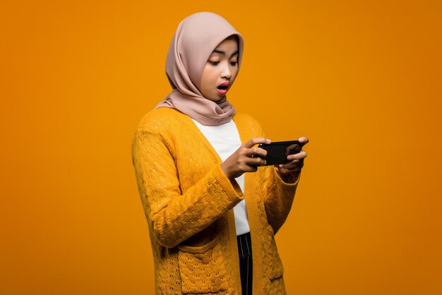 Portrait de la belle femme asiatique jouant un jeu vidéo sur un smartphone avec une expression choquée