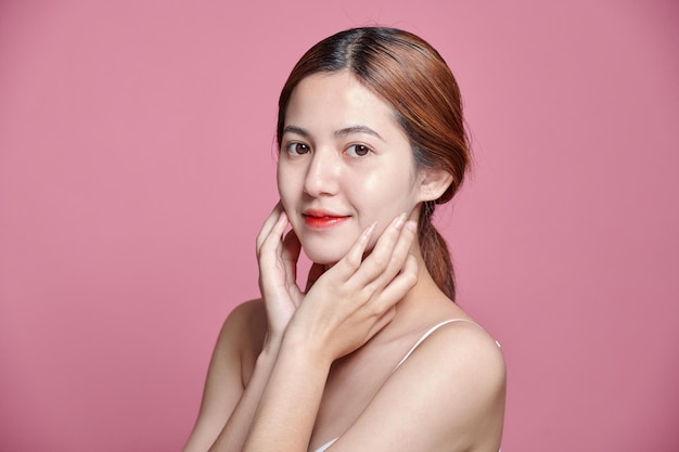Portrait d'une belle femme asiatique avec une peau jeune, propre et en bonne santé, prise en studio sur un fond rose isolé.