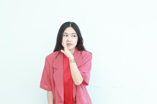 Photo portrait d'une belle femme asiatique portant une tenue rouge avec un geste de chuchotement