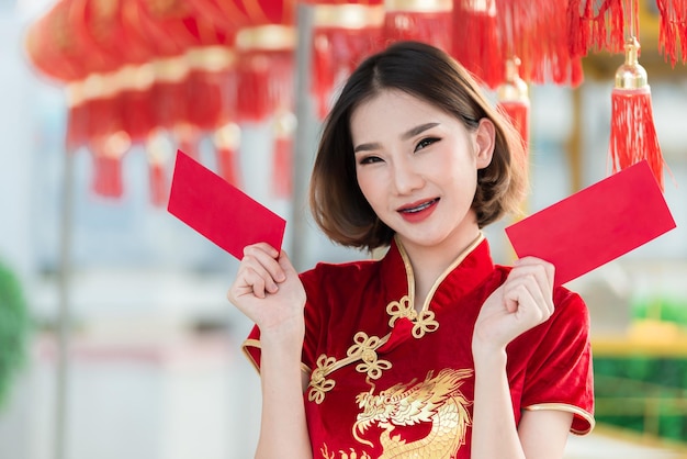 Portrait belle femme asiatique en robe CheongsamThailand peopleHappy Chinese new year conceptHappy asian lady in Chinese traditional dress holding a red enveloppe