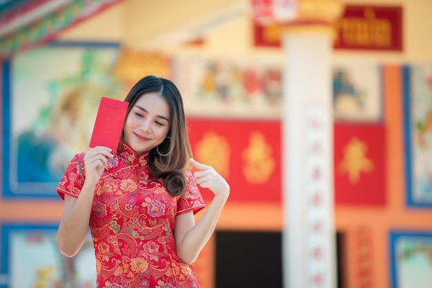 Portrait d'une belle femme asiatique en robe CheongsamThailand peopleHappy Chinese new year conceptHolding enveloppe rouge rouge