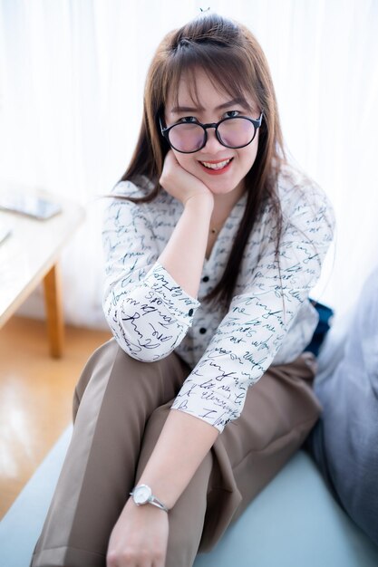 Photo portrait d'une belle femme asiatique souriante et heureuse qui se détend assise sur un canapé confortable