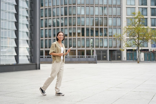 Portrait d'une belle femme asiatique souriante marchant dans la rue du centre-ville avec un smartphone regardant la caméra