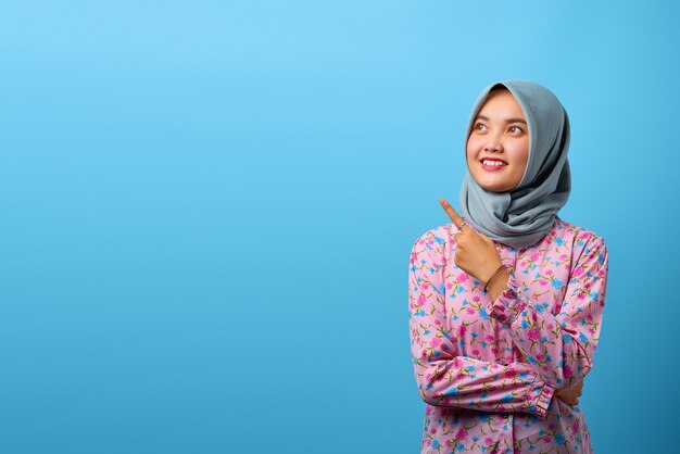 Portrait d'une belle femme asiatique souriante et pointant vers l'espace de copie sur fond bleu