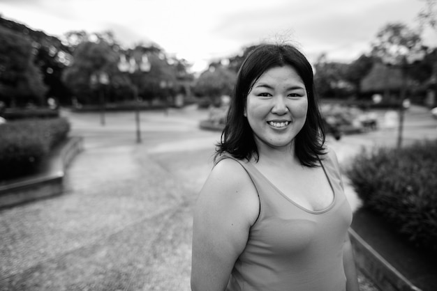 Portrait de la belle femme asiatique en surpoids se détendre dans le parc de la ville en noir et blanc