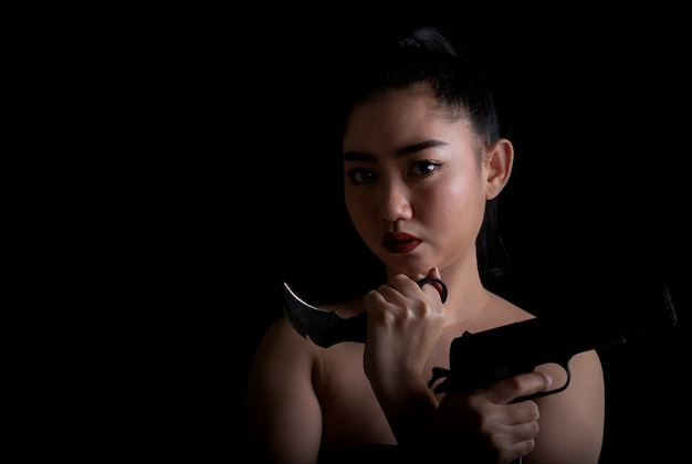 Portrait belle femme d'Asie une main tenant une arme à feu et un couteau karambit sur fond noir