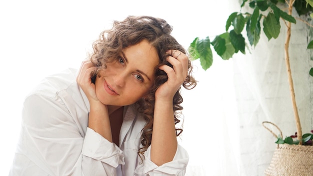 Portrait d'une belle femme assise à la maison avec des plantes et souriant à la caméra. Bonne matinée - journée ensoleillée