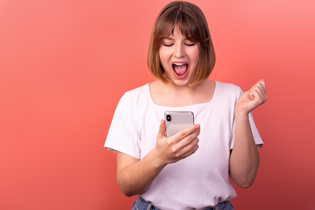 Portrait d'une belle femme aux cheveux bruns joyeuse et étonnée utilisant un appareil téléphonique 5g comme réaction heureuse