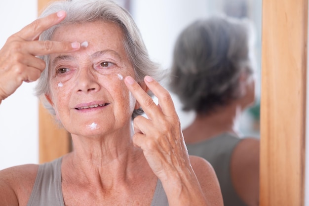 Portrait d'une belle femme aux cheveux gris senior applique une crème anti-âge sur le visage ridé prendre soin du concept de peau