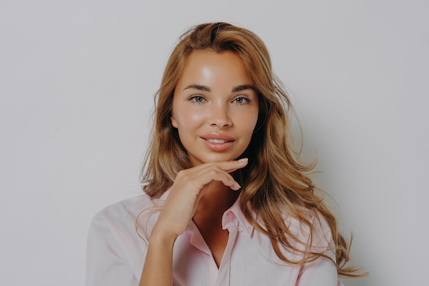 Portrait d'une belle femme aux cheveux longs, une peau saine, un maquillage minimal touche doucement le menton