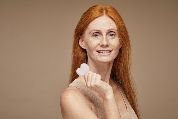 Portrait d'une belle femme aux cheveux rouges avec des taches de rousseur souriant et tenant un espace de copie pour le masseur de visage