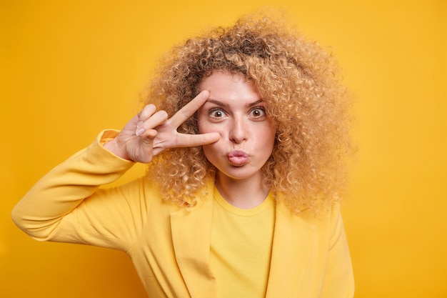 Photo portrait de belle femme aux cheveux touffus bouclés garde les lèvres pliées fait un geste de paix sur les yeux