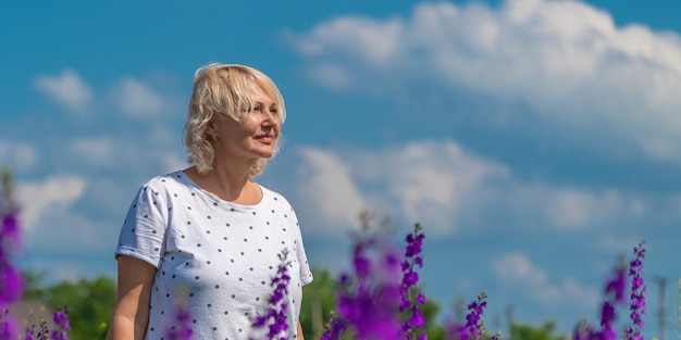 Portrait d'une belle femme blonde d'âge moyen heureuse dans un champ avec un ciel bleu de fond de fleurs