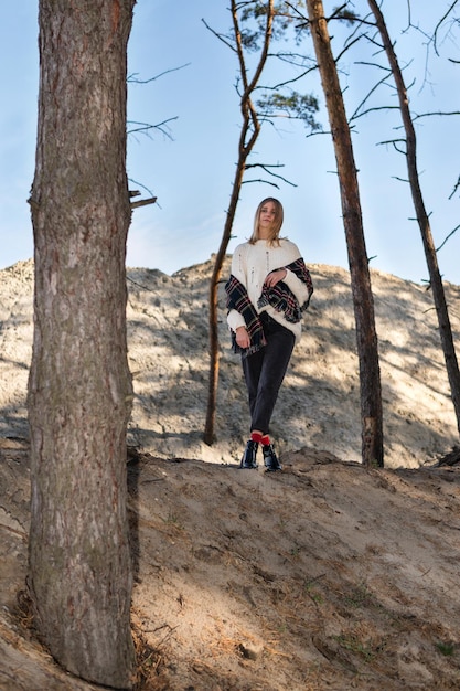 Portrait d'une belle femme blonde en chandail et chalet sur une colline de sable dans une pinède