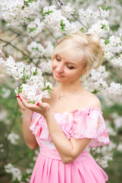 Portrait d'une belle femme blonde dans une robe rose dans un jardin fleuri au printemps.