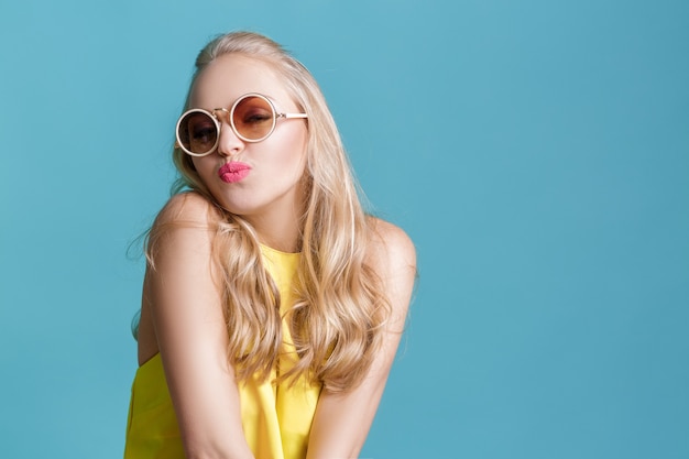 Portrait de belle femme blonde à lunettes de soleil et chemise jaune sur fond bleu été insouciant