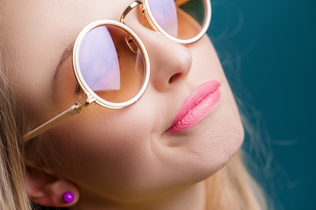 Portrait de belle femme blonde à lunettes de soleil sur fond bleu été insouciant se bouchent