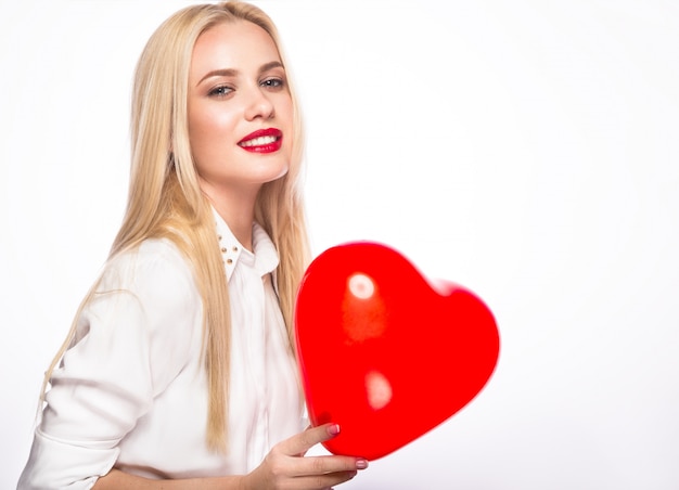 Portrait de la belle femme blonde avec maquillage lumineux et coeur rouge à la main