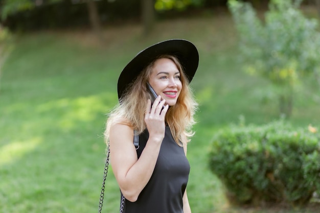 Portrait d'une belle femme à bretelles portant un chapeau parlant au téléphone à l'extérieur