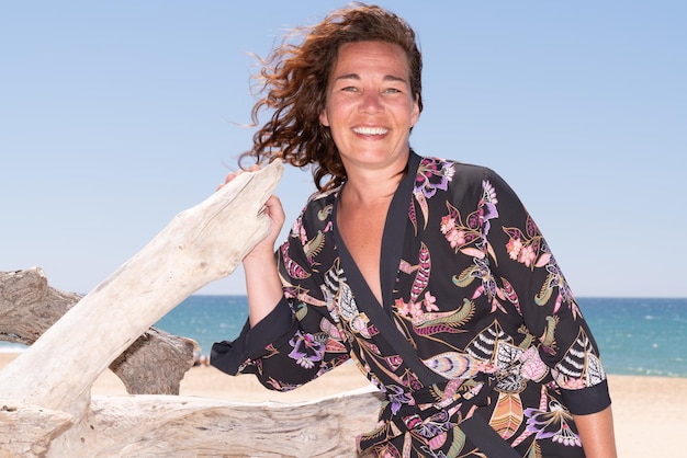 Portrait d'une belle femme brune de 40 ans sur la plage avec du bois flotté