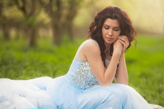 Portrait d'une belle femme brune bouclée assise dans un jardin de fleurs d'arbres